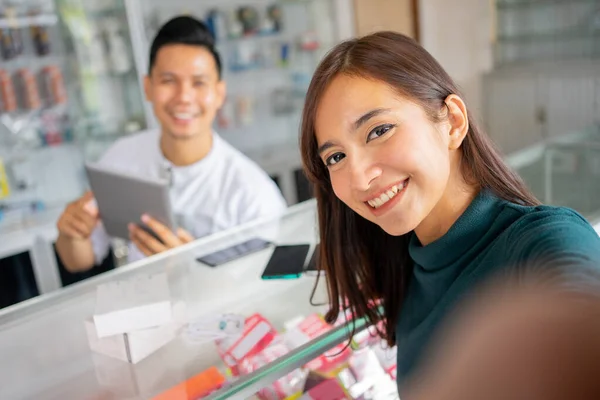 A beautiful woman smiles at the camera while taking a selfie sitting with the back of a man sitting — Stock Photo, Image