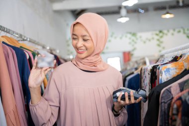 Elinde kredi kartı ve elektronik veri yakalama makinesi olan peçeli bir kız gülümsüyor.