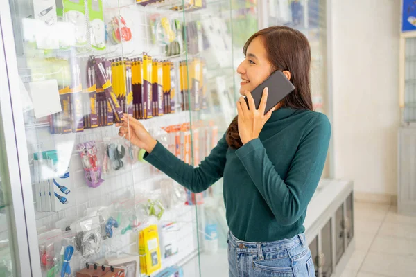 Mulher bonita fazendo uma chamada com um smartphone ao escolher acessórios de telefone celular em uma vitrine — Fotografia de Stock