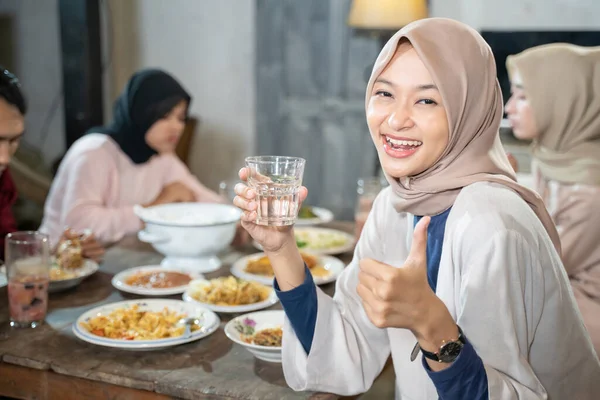 Seorang wanita berkerudung tersenyum di kamera dengan jempol sambil memegang gelas untuk memecahkan cepat — Stok Foto