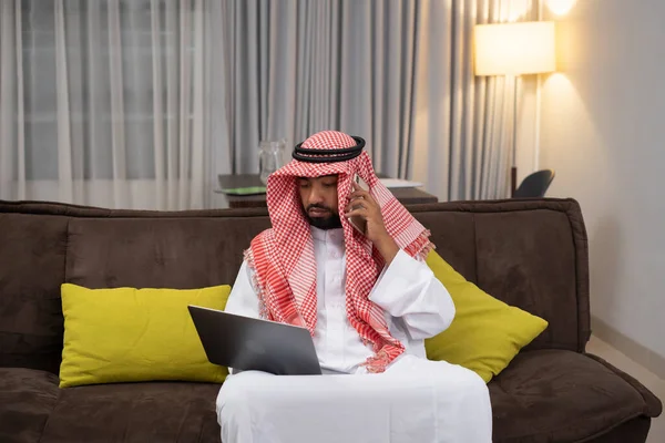 Homme d'affaires arabe dans un turban travaillant à l'aide d'un ordinateur portable et passer des appels téléphoniques tout en étant assis — Photo