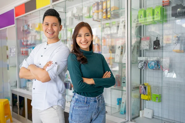 Homem bonito e mulher bonita sorrindo com as mãos cruzadas perto de acessórios de telefone celular vitrine — Fotografia de Stock