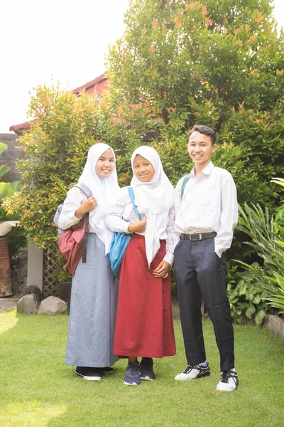 Three smiling teenagers in school uniforms carrying school bags — Stock Photo, Image