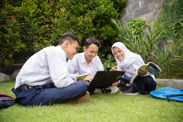 Tre adolescenti in divisa scolastica seria studiano insieme usando un computer portatile mentre sono seduti — Foto Stock