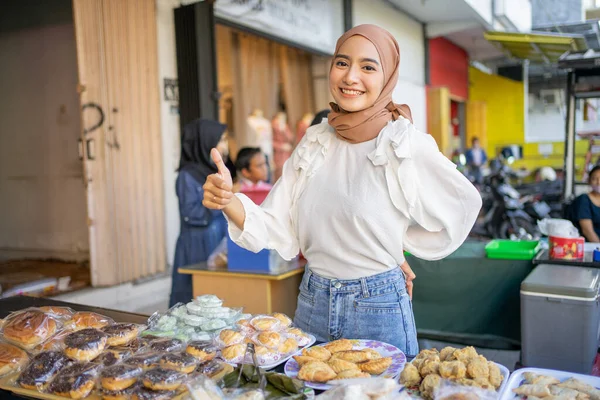 Усміхнена красива дівчина в хіджабі з великими пальцями, пропонуючи різноманітні смажені продукти — стокове фото