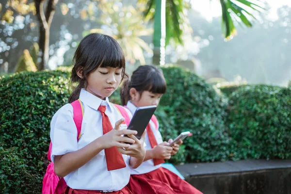 Asiático estudante primário usando telefone celular no parque escolar — Fotografia de Stock