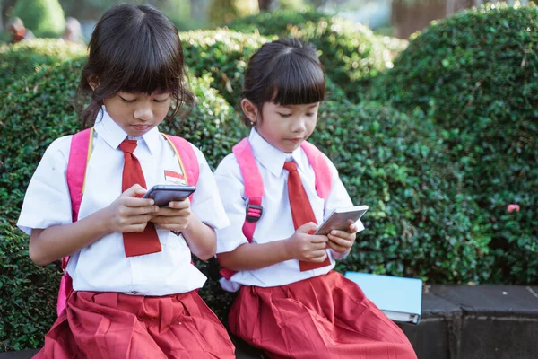 Asian primary student using mobile phone in school park — Stock Photo, Image