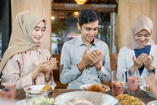 Un hombre y dos mujeres en velo rezan juntos antes de comer mientras rompen su ayuno —  Fotos de Stock
