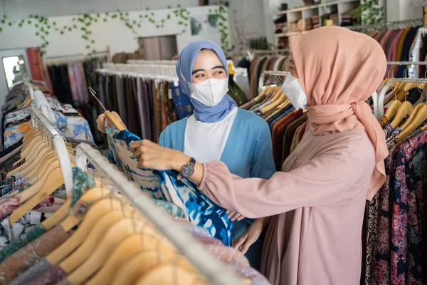 Závoj servírky nosit masky, zatímco slouží ženské nakupující výběr oblečení — Stock fotografie