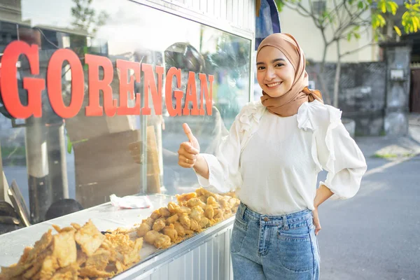 Egy gyönyörű lány egy fátyolban, hüvelykujjával felfelé, különféle sült ételeket árul egy szekérrel. — Stock Fotó