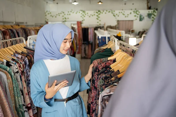 Obchodní žena v modrém závoji s použitím tabletu, zatímco drží oblečení na ramínku — Stock fotografie