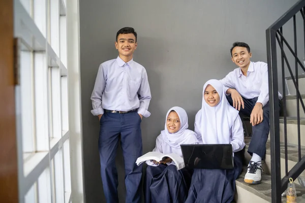 Fyra tonåringar i junior gymnasiet uniformer ler mot kameran medan du håller en bärbar dator och en bok — Stockfoto