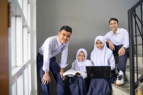 En grupp tonåringar i junior high school uniformer ler mot kameran medan du håller en bärbar dator och en bok — Stockfoto