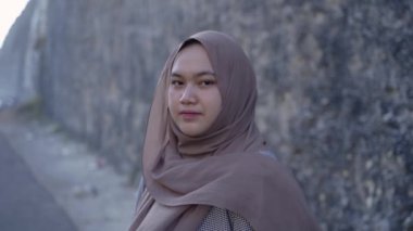 Kafasını örten tesettürlü kız, kumsalda mutluluktan sırıtıyor.