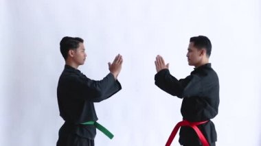 Pencak silat üniforması giyen iki Asyalı adam karşılıklı saygıyla karşı karşıya duruyor.