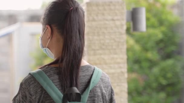 A teenage girl standing wearing a mask and backpack carrying a book — Stock video