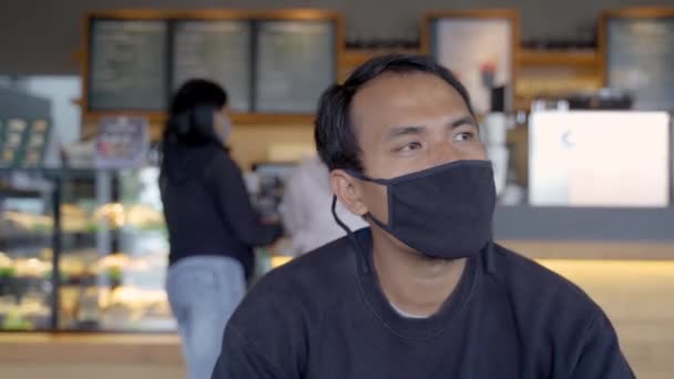 Kafede bekleyen bir adam maskesiyle kahvenin tadını çıkarıyor. — Stok video