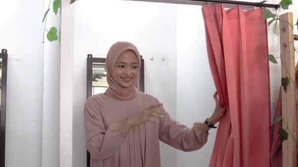 A beautiful girl in a veil trying on clothes in a changing room in front of the mirror and her friend complimented her with a thumbs up — Stock Video