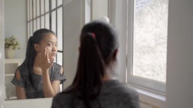 Asyalı Kız 'ın aynaya bakarken deriyle ilgili sorunları var. Endişeli genç bayan.