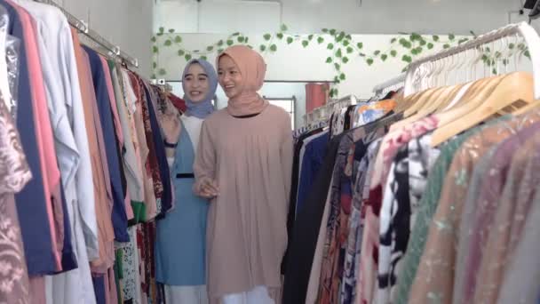 Asian veiled waitresses while serving female shoppers choosing clothes on hangers — Stock Video