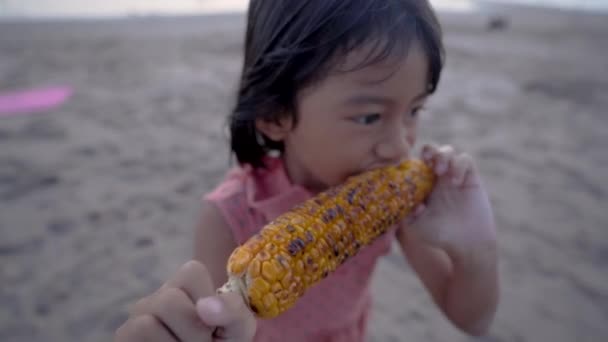 Очаровательная забавная девушка ест кукурузу в початках в солнечный летний день — стоковое видео