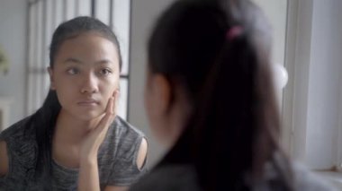 Asyalı Kız 'ın aynaya bakarken deriyle ilgili sorunları var. Endişeli genç bayan.