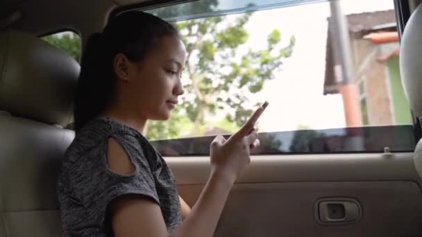 Азиатка улыбается, когда держит телефон, сидя в машине — стоковое видео