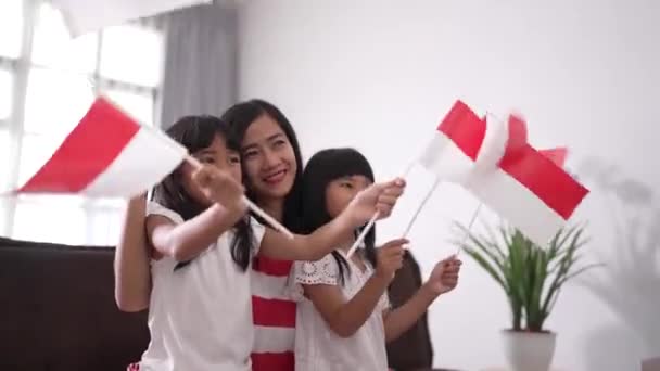 Ibu dan anak merayakan kemerdekaan indonesia hari di rumah mengenakan merah dan putih dengan bendera indonesia — Stok Video