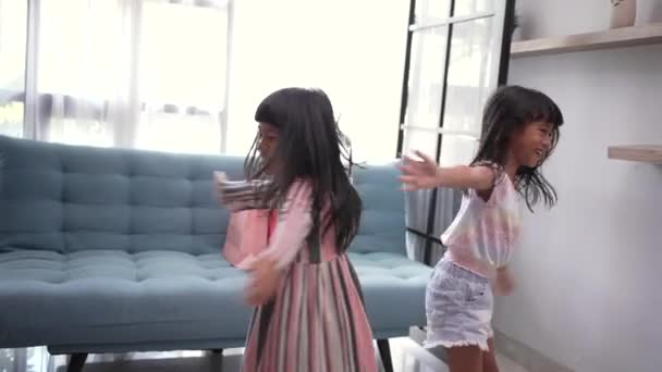 Šťastné roztomilé asijské malé holky sestra nebo přátelé baví hrát spolu v kuchyni. Dvě zábavné děti krouží, skákají, zpívají v obývacím pokoji — Stock video