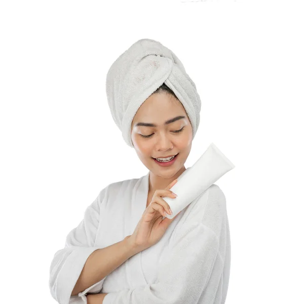 Beautiful woman in towel holding white tube bottle beside shoulder — стоковое фото