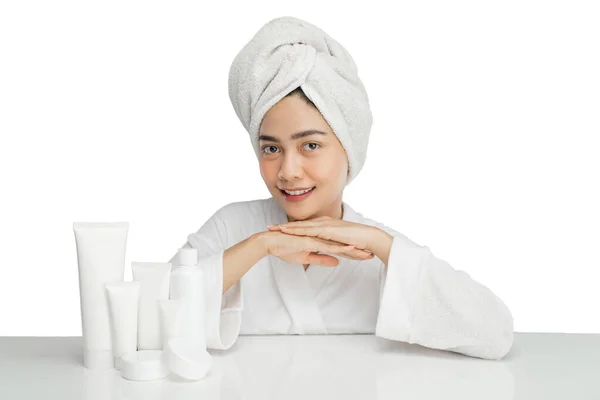 Girl model with towel on her head sitting with various skin care products on table — Foto Stock