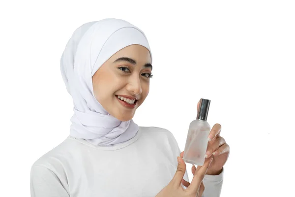 Smiling asian hijab woman wearing white dress holding a bottle of facial care serum — Fotografia de Stock