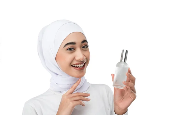 Excited asian hijab girl wearing white dress holding a bottle of serum with hands gesture — стоковое фото