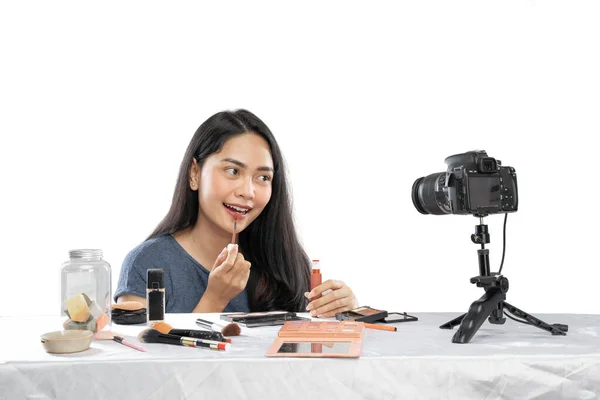 Jonge glimlachende vrouwelijke video blogger met behulp van lippenstift met tonen cosmetische product naar camera — Stockfoto