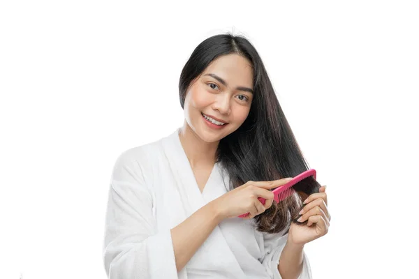 在用梳子梳理长发时，亚洲女人头戴毛巾看着相机 — 图库照片