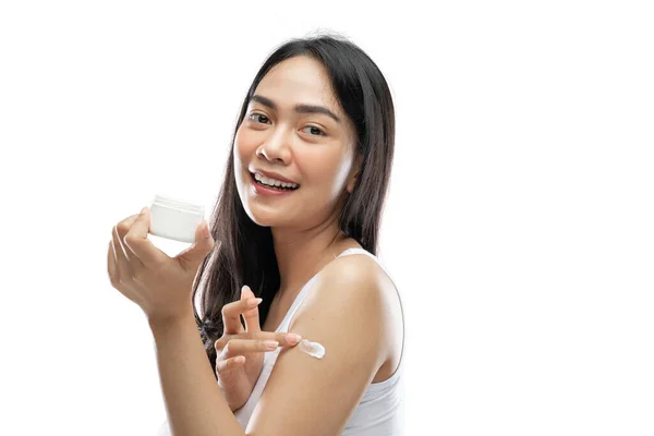 Smiling asian woman wearing white underdress using body cream rub into arm — Photo