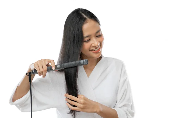 A smiling woman wearing a towel uses a hair straightener — Stok fotoğraf