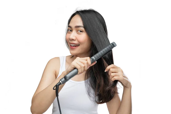 A smiling woman wearing underdress uses a hair straightener to straighten — Stockfoto