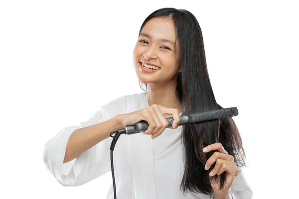 Smiling woman straightening hair with hair straightener — Stok fotoğraf