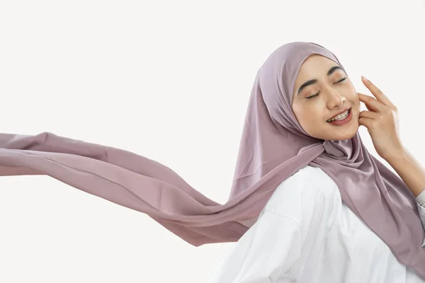 Hijab girl enjoying wearing a purple veil waving in the wind with a hand gesture on the cheek — Stockfoto