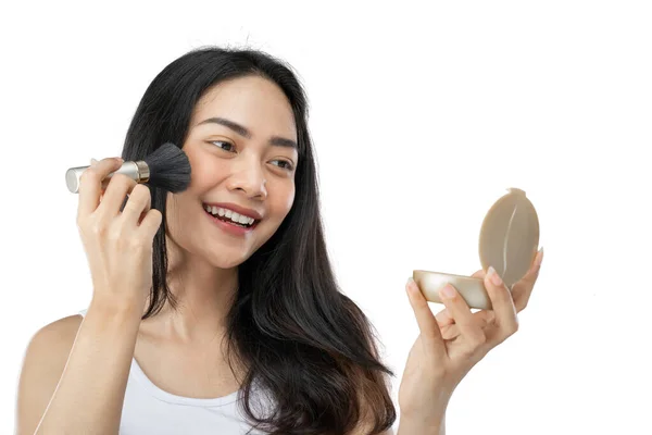 Young beautiful woman with long black hair using brush to wipe powder on cheeks while holding small mirror — Photo