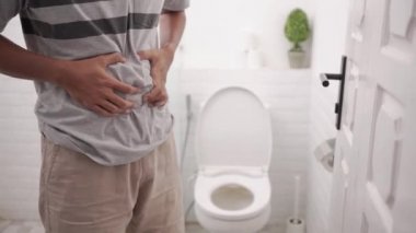 Midesi ağrıyan bir erkek tuvalette ishal oluyor ve karnını acı içinde tutuyor..