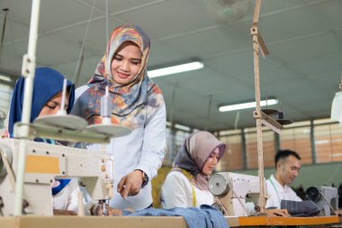 female supervisor in a veil with a pointing finger is standing at the side and sees the seamstress using the sewing machine