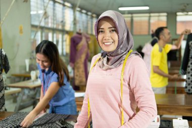 Veiled women tailor smiling when standing with tape measure worn around the neck