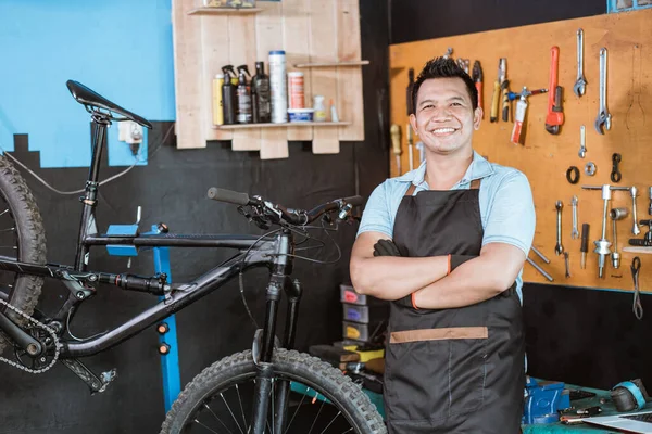 A bicycle mechanic wearing an apron and gloves smiles with crossed hands — Stock fotografie