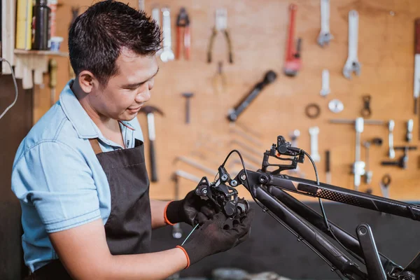 A mechanic wearing an apron and gloves installs the rear derailleur with cable — Φωτογραφία Αρχείου