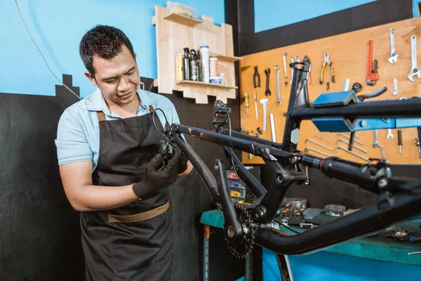 A bicycle mechanic in apron holds the rear mech as it attaches to the frame — Stock fotografie