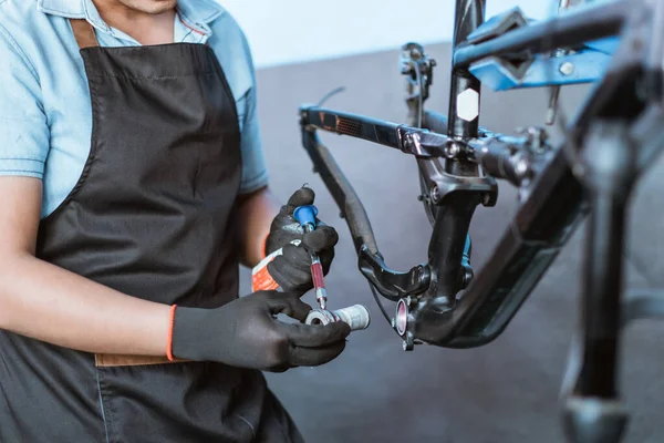 The hands of a young mechanic wearing gloves holding the bottom bracket to be lubricated with oil — Fotografia de Stock