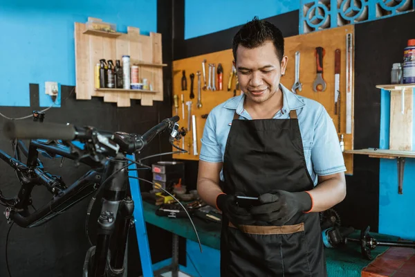 Portrait of a repairman in an apron using a cellphone while repairing a bicycle — Stock fotografie