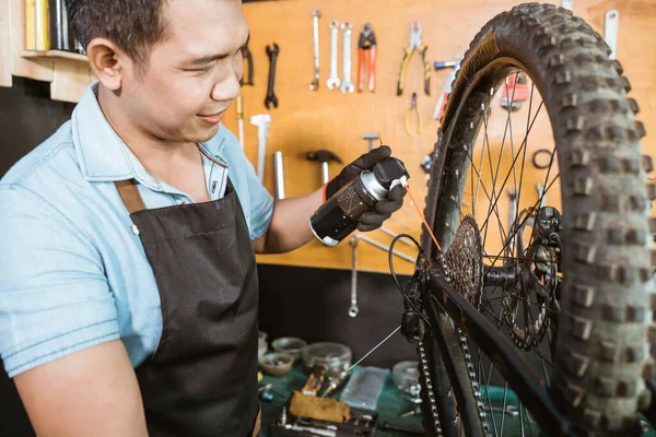 Mecânico de bicicletas macho em garrafa de avental enquanto aplica spray de lubrificante — Fotografia de Stock